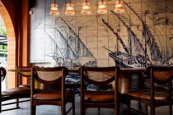 A decoração usa tons terrosos nas paredes, mural de azulejos com caravelas e quadros com receitas de família, além de iluminação intimista: A decoração usa tons terrosos nas paredes, mural de azulejos com caravelas e quadros com receitas de família, além de iluminação intimista: